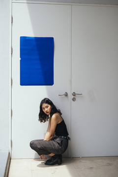 黑色卷曲长发女孩以别致的姿势坐在门前用蓝色的纸，坐在明暗之间。