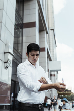 成熟的亚洲商务人士穿着白色正式衬衫，右臂在办公室外卷起袖子。