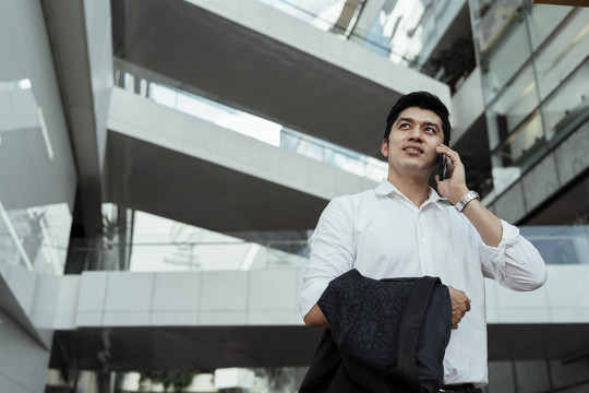 穿着白色正式衬衫的成熟亚洲商人在街上用智能手机交谈。