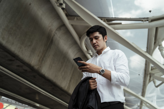 穿着白色正式衬衫的成熟亚洲商人在街上使用智能手机。