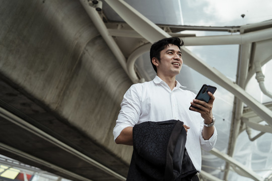 穿着白色正式衬衫的成熟亚洲商人在街上使用智能手机。