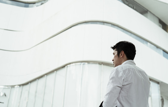 穿着白色正式衬衫的成熟亚洲商人看着曼谷市的白色建筑。