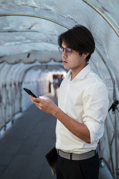 一个穿白衬衫的黑发男人在收到朋友的通知时会看他的智能手机。