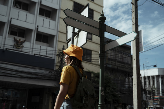 在夏日的阳光下，背着绿色背包的黄色背包女站在路边的路标旁。