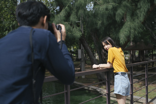 男摄影师拍了一张十几岁的女模特站在公园里的小桥上和坐在桥上的照片。