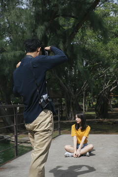 男摄影师拍了一张十几岁的女模特站在公园里的小桥上和坐在桥上的照片。