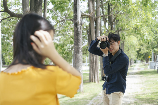 男摄影师在公园里的走道上给少女模特拍照，并把树叶送给她做道具。