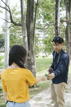 男摄影师在公园里的走道上给少女模特拍照，并把树叶送给她做道具。