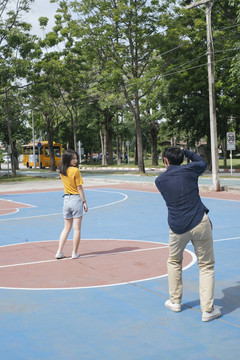 男摄影师为女模特在篮球场上站、跳、坐拍照。