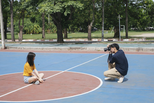 男摄影师为女模特在篮球场上站、跳、坐拍照。