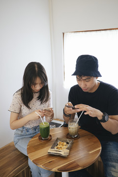 男人和女人坐在咖啡馆里用智能手机拍照。