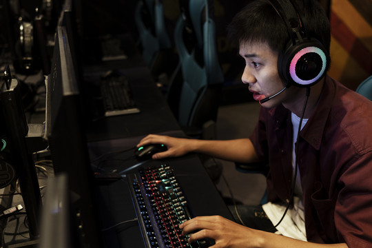 严肃的年轻亚洲游戏玩家在网吧玩电脑游戏，戴着耳机，和朋友聊天。