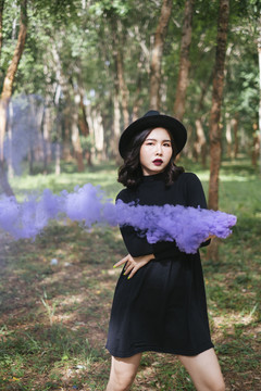 一个黑衣女巫在森林里玩紫烟手电筒。