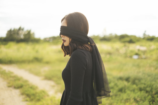 站在田野里的黑色新娘，戴着用面纱做的眼罩。