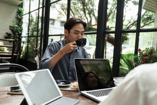 年轻的商人在继续开会前喝咖啡。拿着一杯热咖啡的亚洲年轻人。