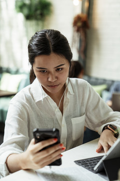年轻的泰国女人在玩智能手机，欣赏音乐，戴上白色耳机。