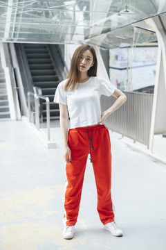 时尚写真-美丽的亚洲年轻女子穿着白衬衫和红色运动裤站着摆姿势。