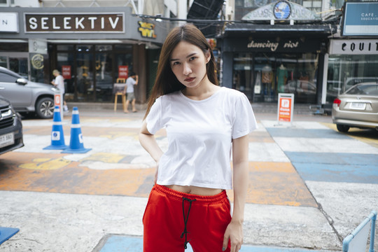 时尚写真-身穿白色衬衫和红色运动裤的泰国亚裔年轻女子站在人行道上。