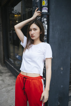 时尚写真-身穿白色衬衫和红色运动裤的泰国亚裔年轻女子斜靠在波兰街上。