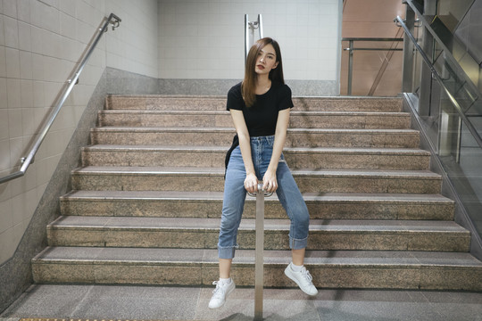 全长时尚写真-美丽的亚洲年轻女子穿着黑色衬衫和牛仔裤长裤坐在地下楼梯。