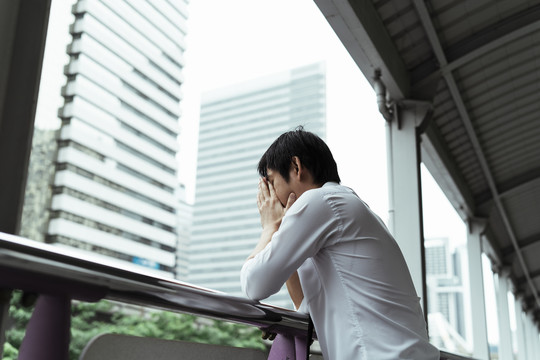 悲伤的泰国年轻商人站在天桥上，双手靠在扶手上望着外面的路。辞职后的泰国年轻人生意压力很大。