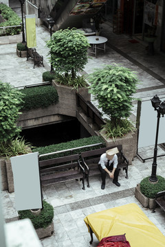 坐在城市花园广场长椅上的纸袋男。孤独的纸袋人独自坐在城市里。