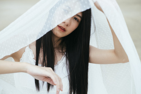 年轻的亚洲长发黑发女子新娘在户外戴着白色面纱的肖像。