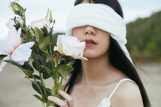 年轻的亚洲长发黑发女子新娘的肖像，戴着白色面纱，在户外捧着白玫瑰。