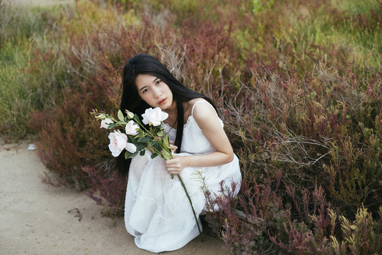 特写-年轻的亚洲长黑发女子新娘手持白玫瑰花坐在田野里的肖像。复古的。