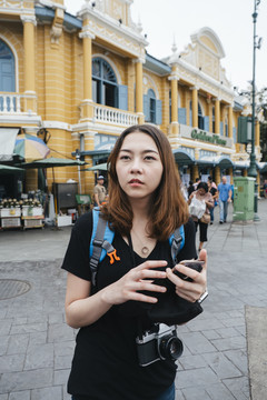 穿黑衬衫的背包女在曼谷用智能手机旅行。