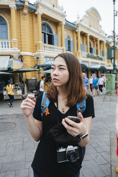 穿黑衬衫的背包女在曼谷用智能手机旅行。