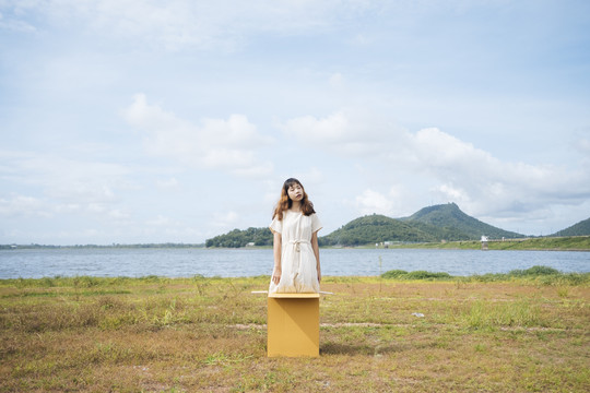年轻的泰国亚裔女子嬉皮卷发的白色礼服站在箱子里在湖边。