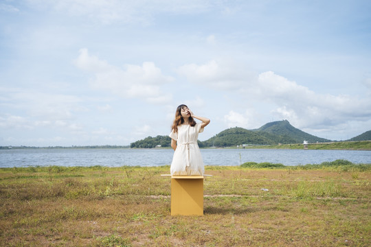 年轻的泰国亚裔女子嬉皮卷发的白色礼服站在箱子里在湖边。