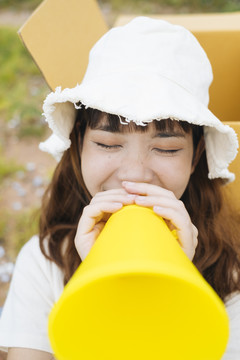 年轻的泰国亚裔女子时髦卷发的白色礼服和帽子说话黄色玩具扩音器。