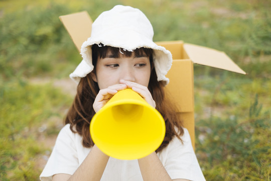 年轻的泰国亚裔女子时髦卷发的白色礼服和帽子说话黄色玩具扩音器。