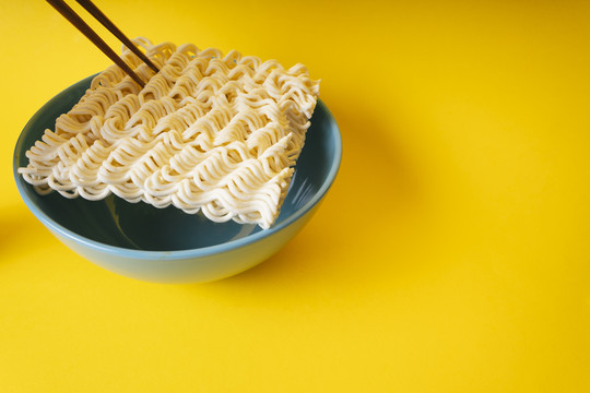 碗里的方便面和黄色背景上的筷子。