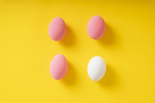 顶视图-三个粉红色的鸡蛋和一个白色的黄色背景。