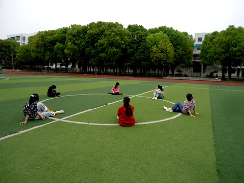 中学生女生坐在足球场聊天
