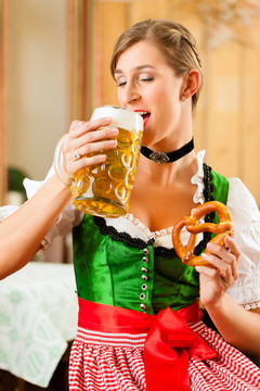 年轻女子在传统的巴伐利亚州餐厅或酒吧里喝啤酒、牛排和椒盐卷饼