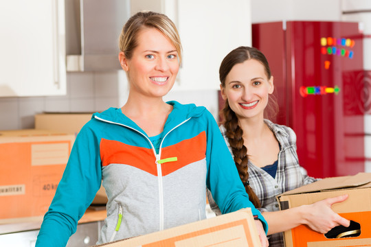 年轻女性——可能是朋友——在家里搬箱子搬进或搬出公寓，专注于搬箱子
