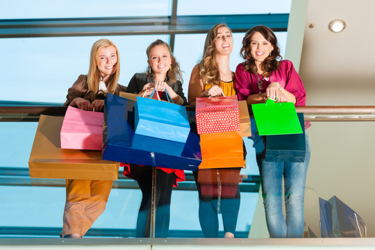 四个带着购物袋的女性朋友在商场购物时玩得很开心