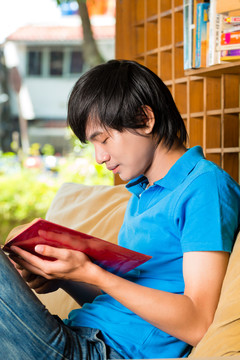 亚洲学生-坐在沙发上看书或学习课本的年轻人