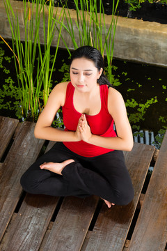 年轻的亚洲女子坐在瑜伽的位置，同时在热带地区冥想