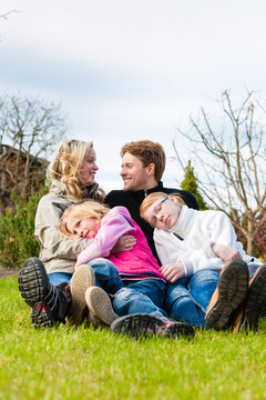 一家人，父亲，母亲和女儿，坐在一起的草地上，他们笑着玩