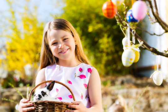 小女孩在春天寻找复活节彩蛋，一只复活节兔子坐在篮子里