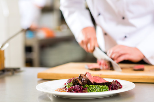 厨师在饭店或餐厅的厨房里做饭，只有双手，他正在切肉或牛排，为盘子上的一道菜