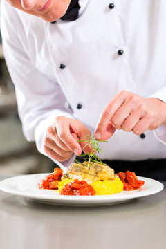 厨师在饭店或饭店的厨房里做饭，他正在盘上完成一道菜