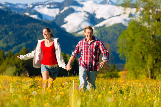 幸福夫妻在山前的草地上奔跑全景