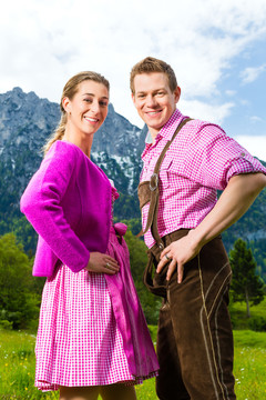 一对身着传统服饰的幸福夫妻站在草地上，山景尽收眼底