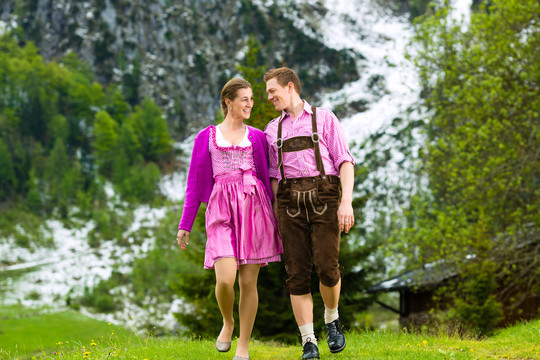 一对身着传统服饰的幸福夫妻漫步在山峦纵横的草地上